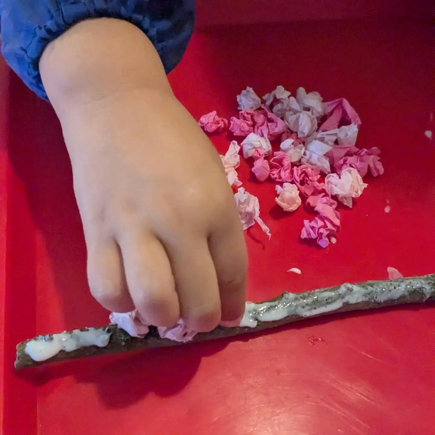 Child's hand attaching crumbled paper to a glue-covered stick