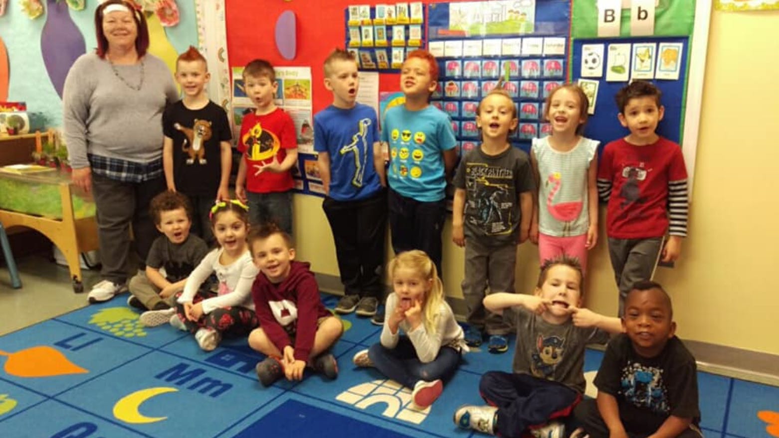 Adult and multiple children posing in a classroom