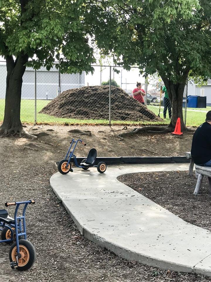 Two pedal cars on a winding concrete path with a pile of mulch in the background