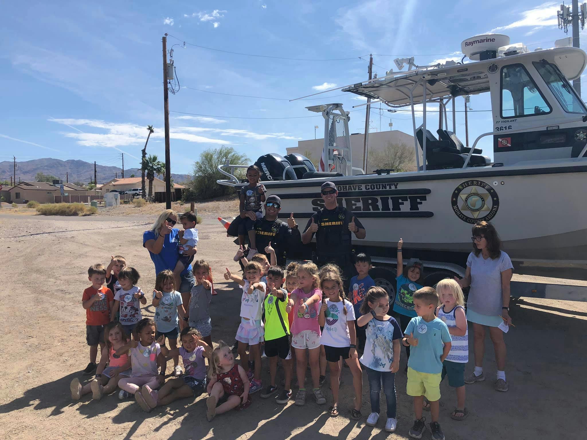 Group of children and adults posing in front of a boat with "SHERIFF" on its side