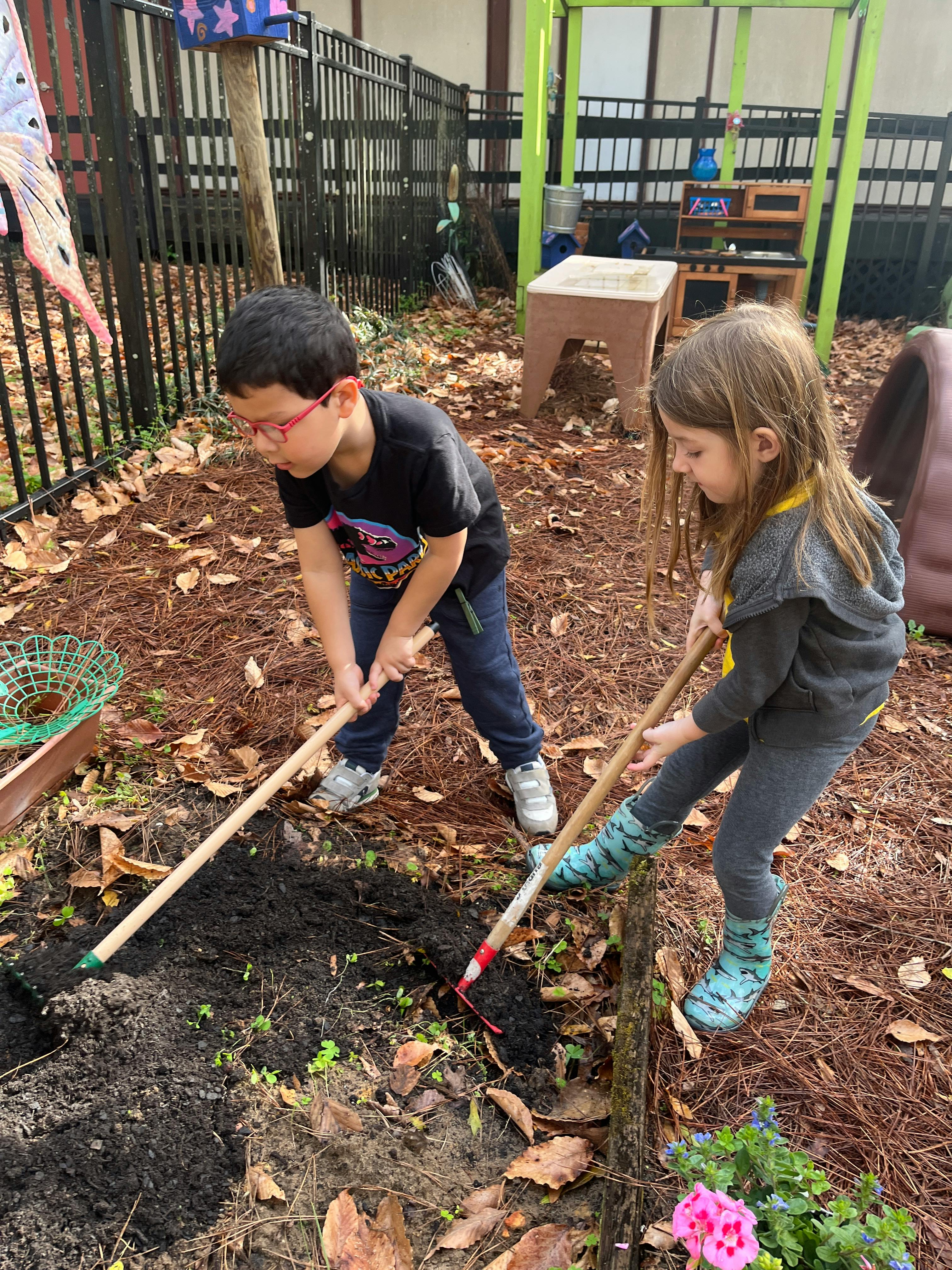Two children digging in dirt with gardening tools