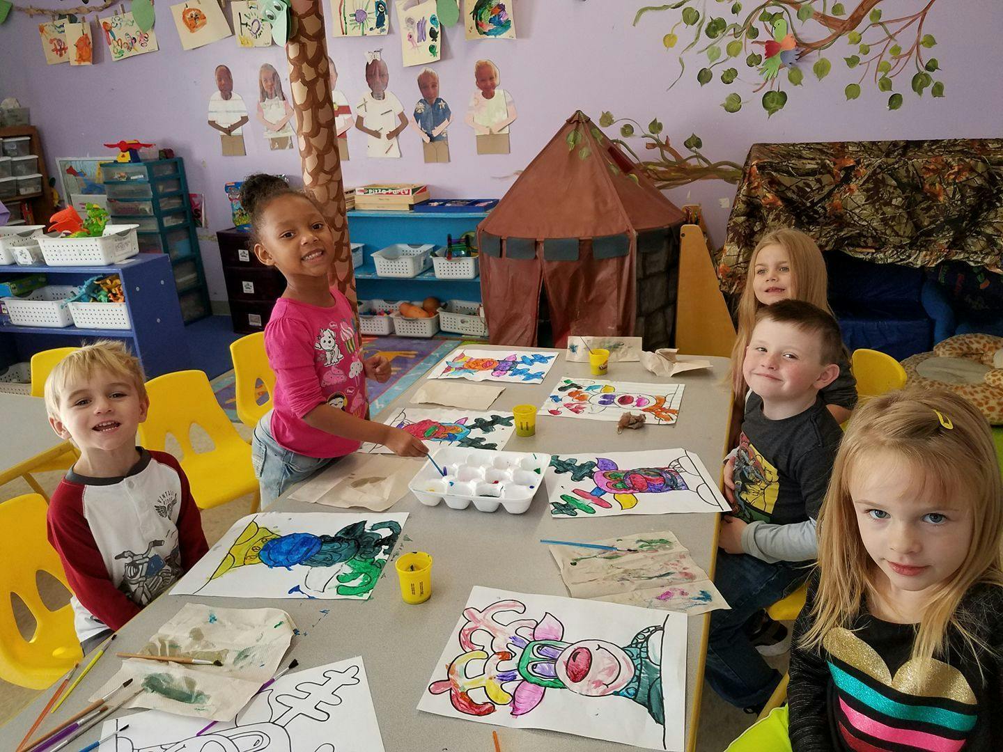 Children sitting at a table with art supplies and drawings