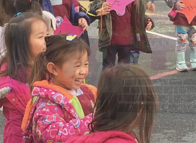 Child in a pink jacket smiling, with other children in the background