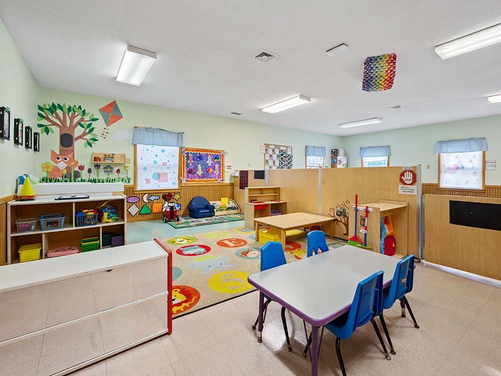Colorful classroom with small tables and chairs, and playful wall decorations