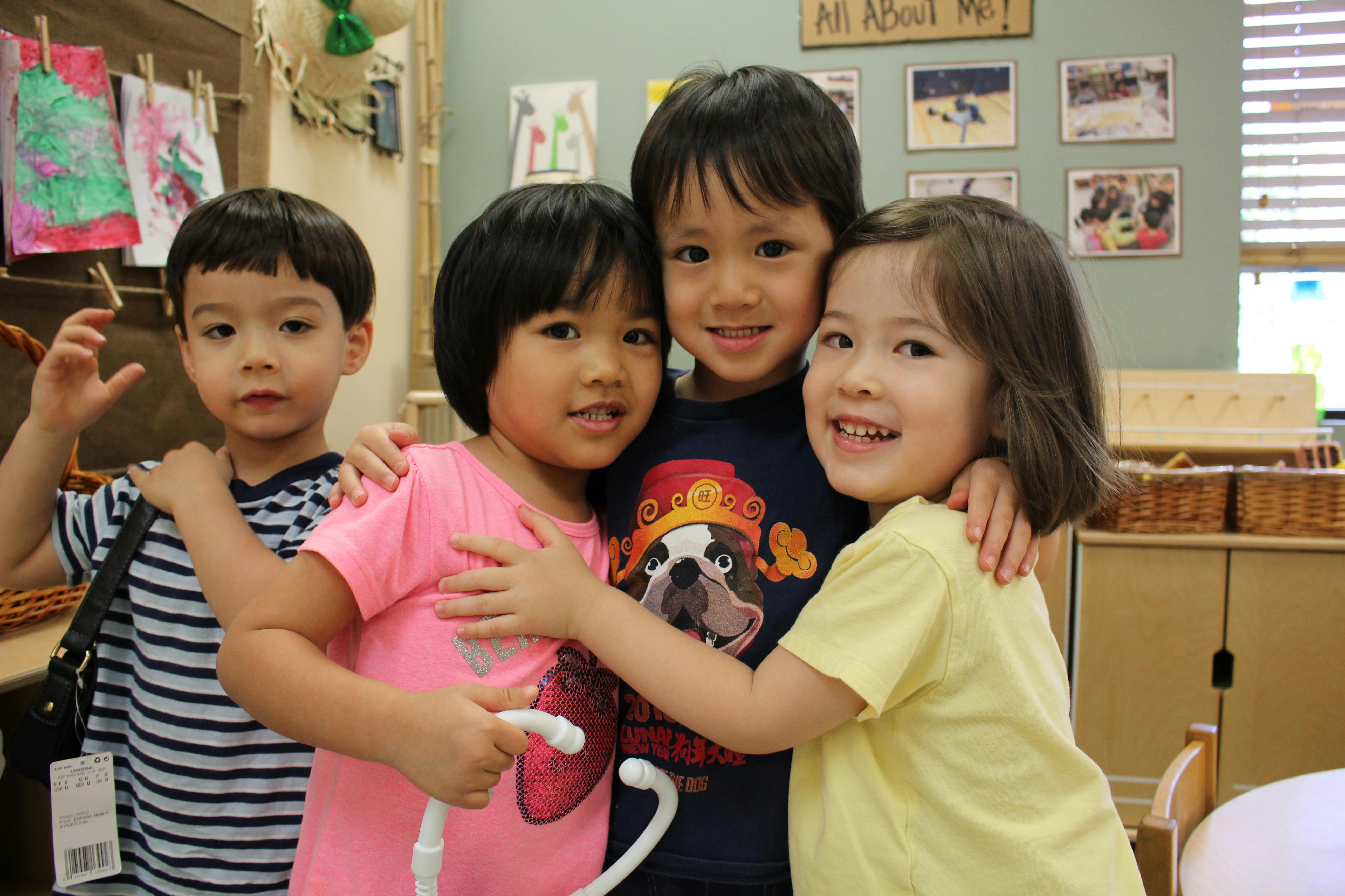 Four children hugging in a classroom