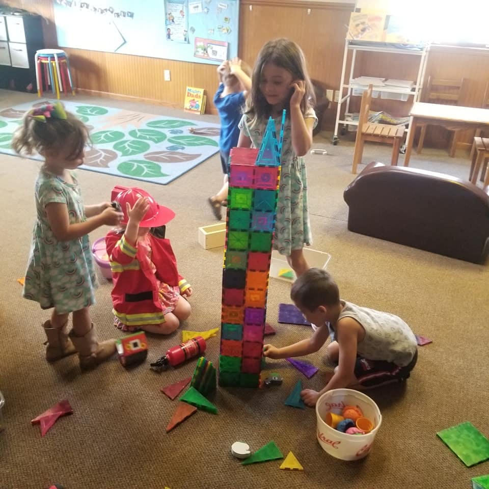 Children playing with magnetic blocks and dress-up clothes in a room
