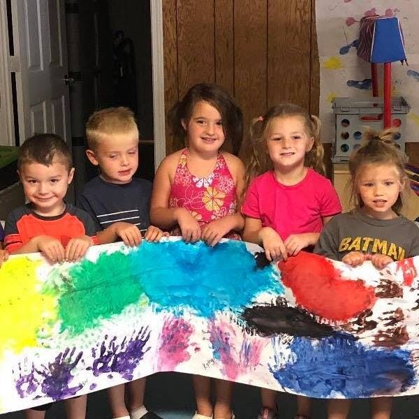 Five children holding up a colorful painted banner with handprints
