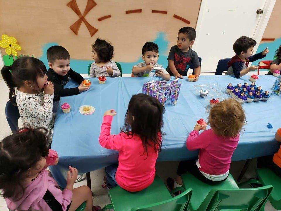 Children sitting around a table with cupcakes and items on it