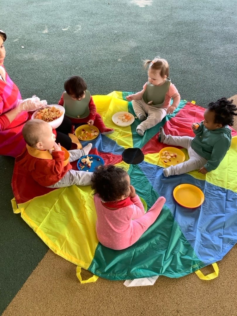 Adult and multiple children sitting on a colorful mat with food
