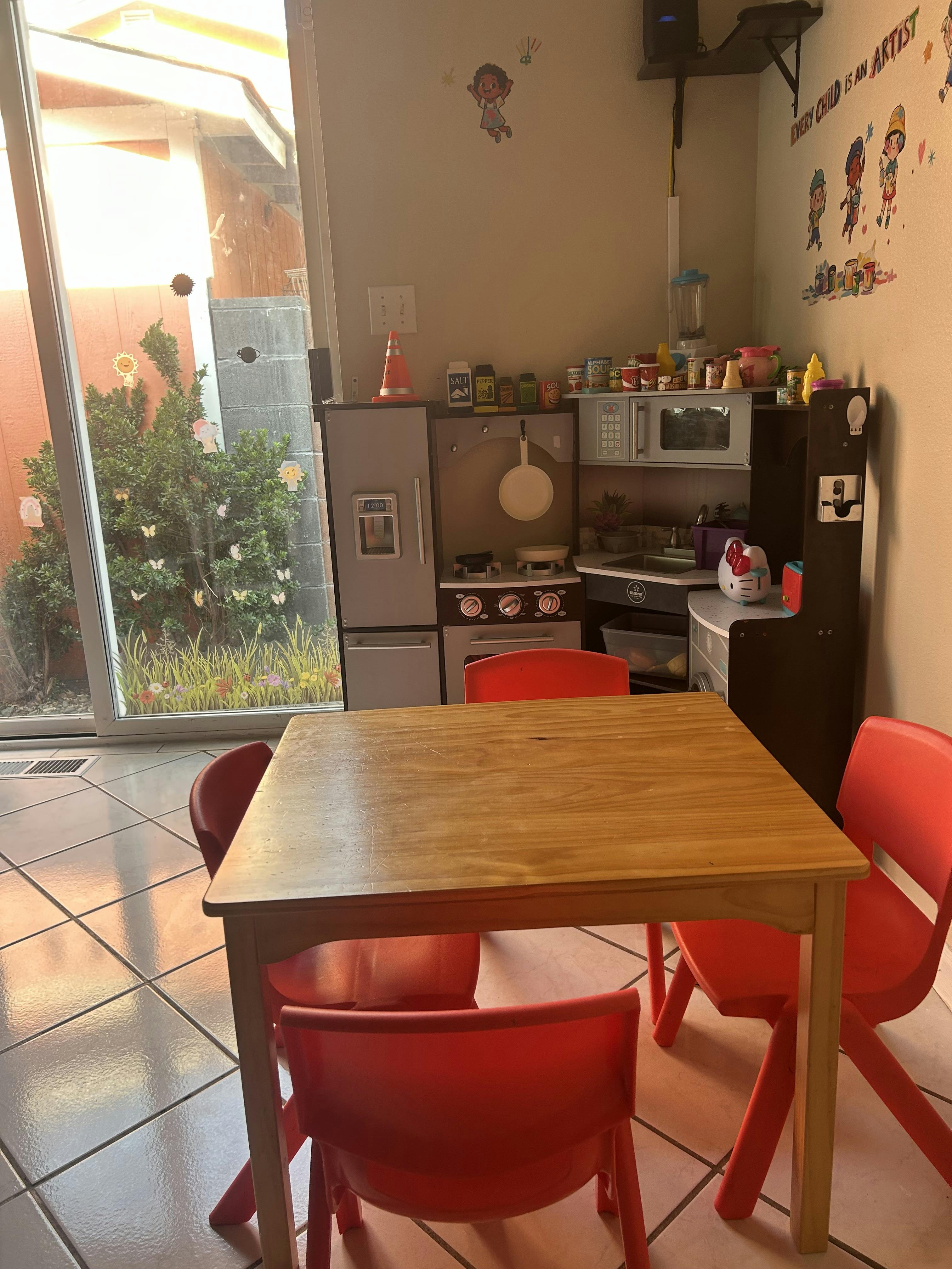 Wooden play kitchen with a small table and red chairs in a room