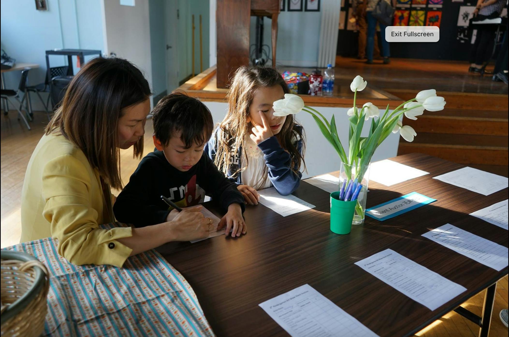 Person and two children at a table with papers and flowers