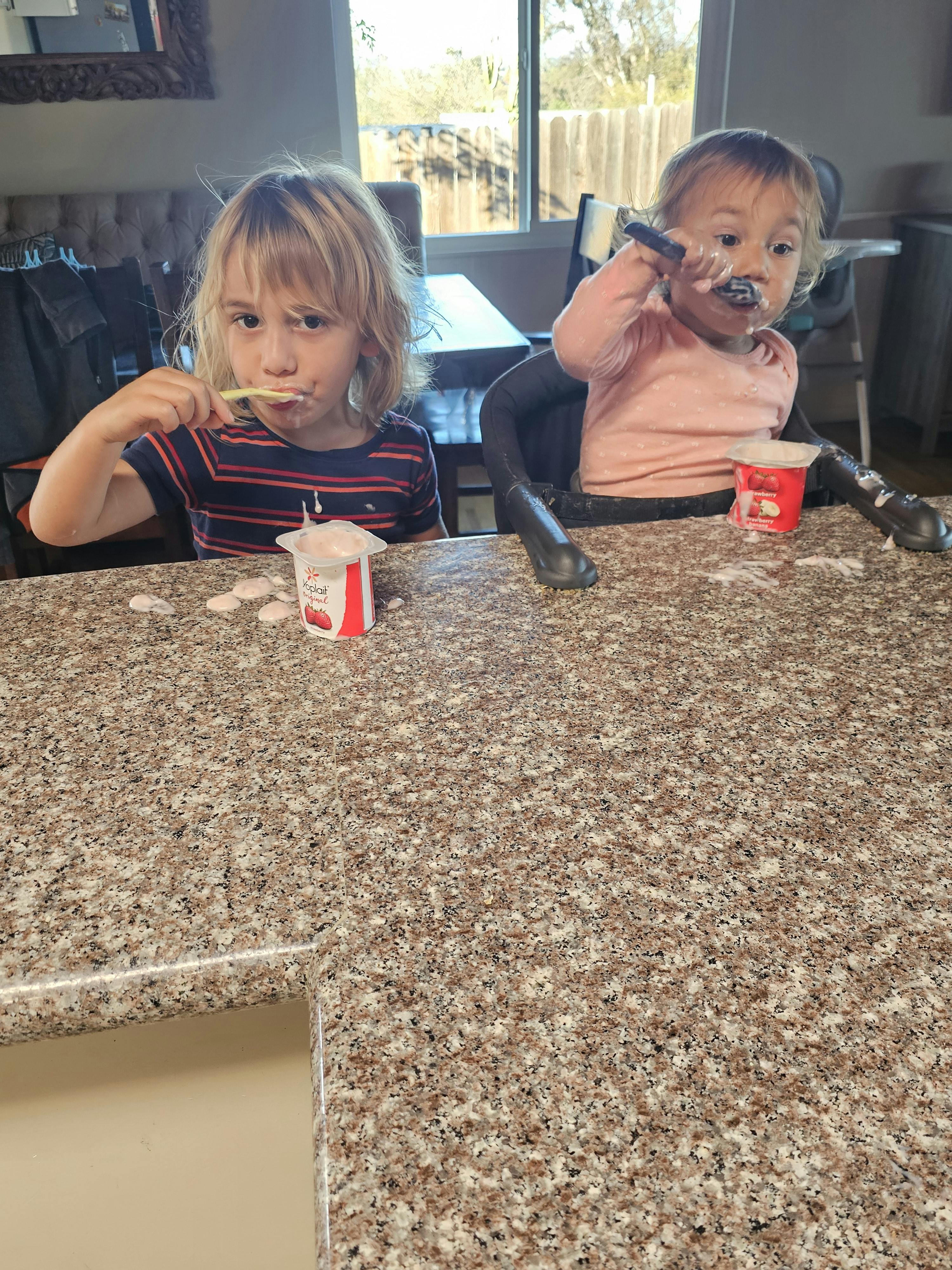 Two children eating yogurt at a counter
