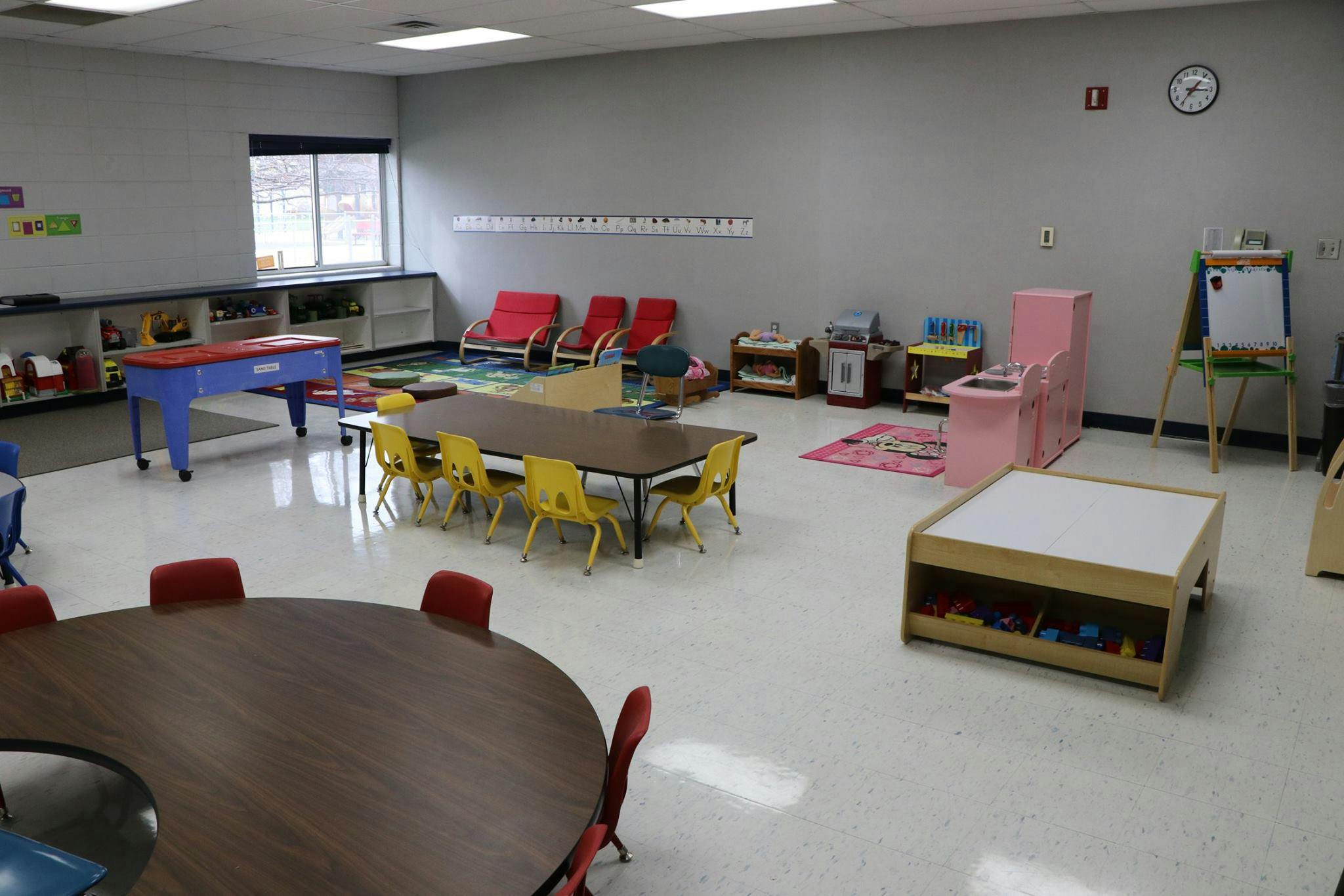 Classroom with tables and chairs, a play kitchen, and an easel