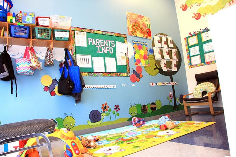 Classroom with a "Parents Info" board, coat hooks, and a colorful playmat
