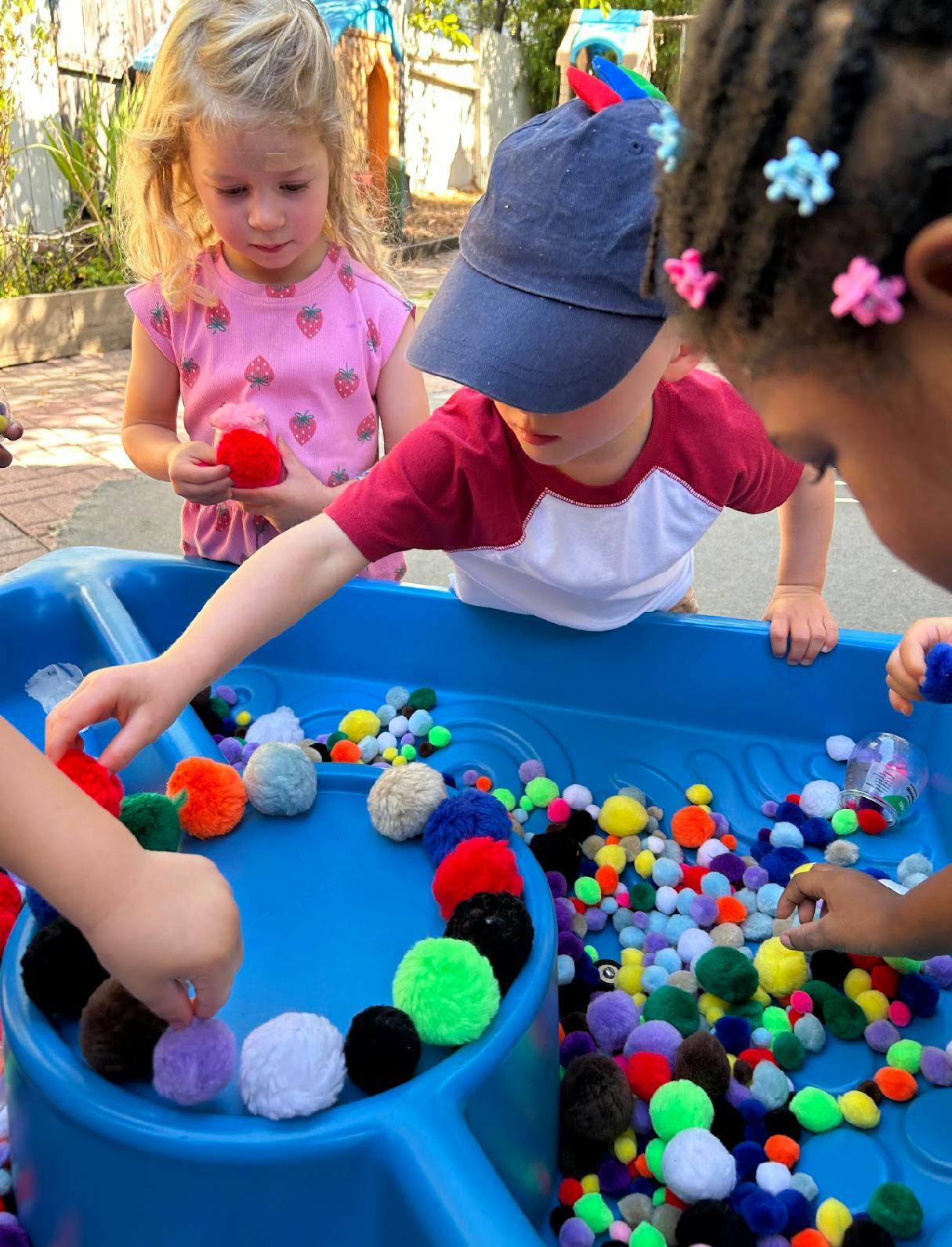 Children playing with colorful pom-poms in a blue sensory table