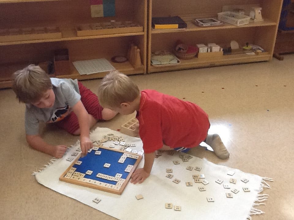Two children on floor playing with letter tiles and a board
