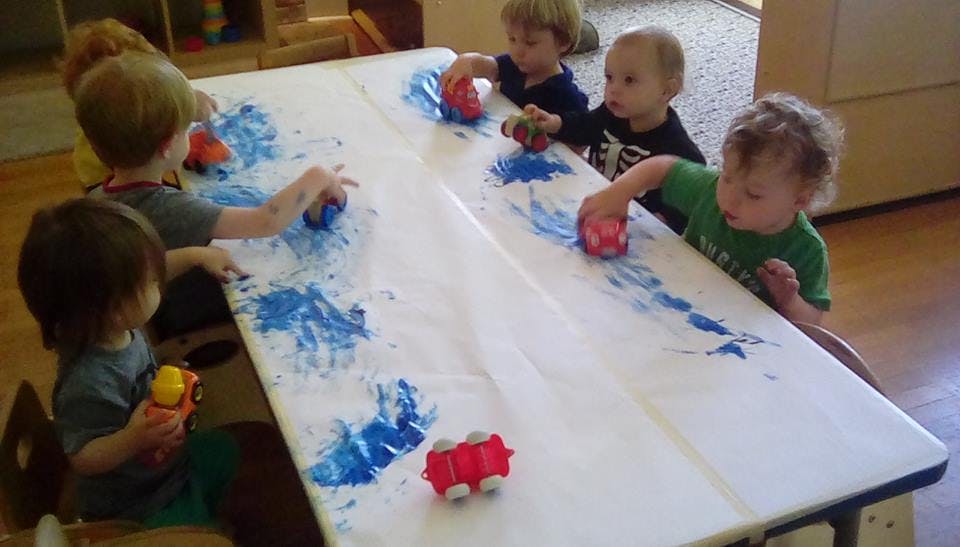 Children playing with toy cars and blue paint on a table