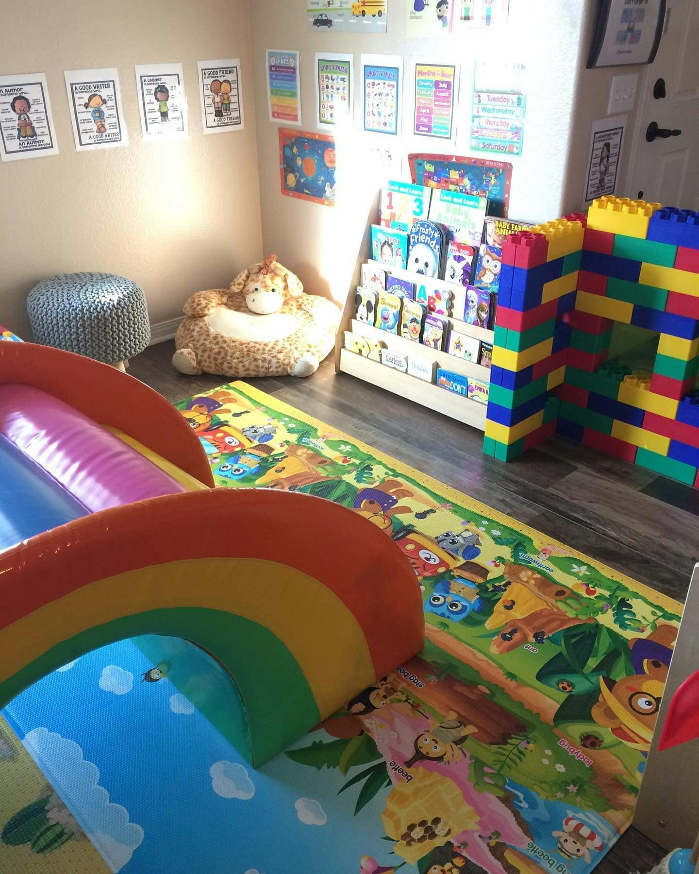 Playroom with an inflatable rainbow slide, book display, and large building blocks