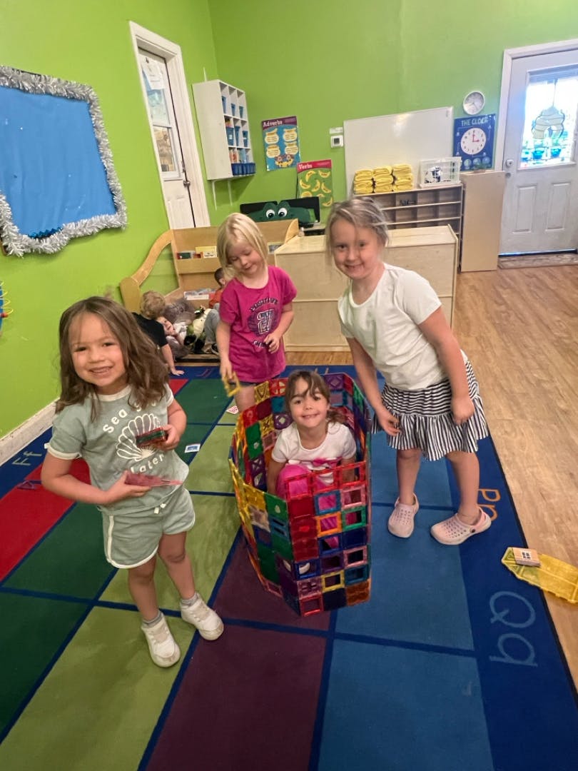 Three children playing in a classroom, one in a colorful box