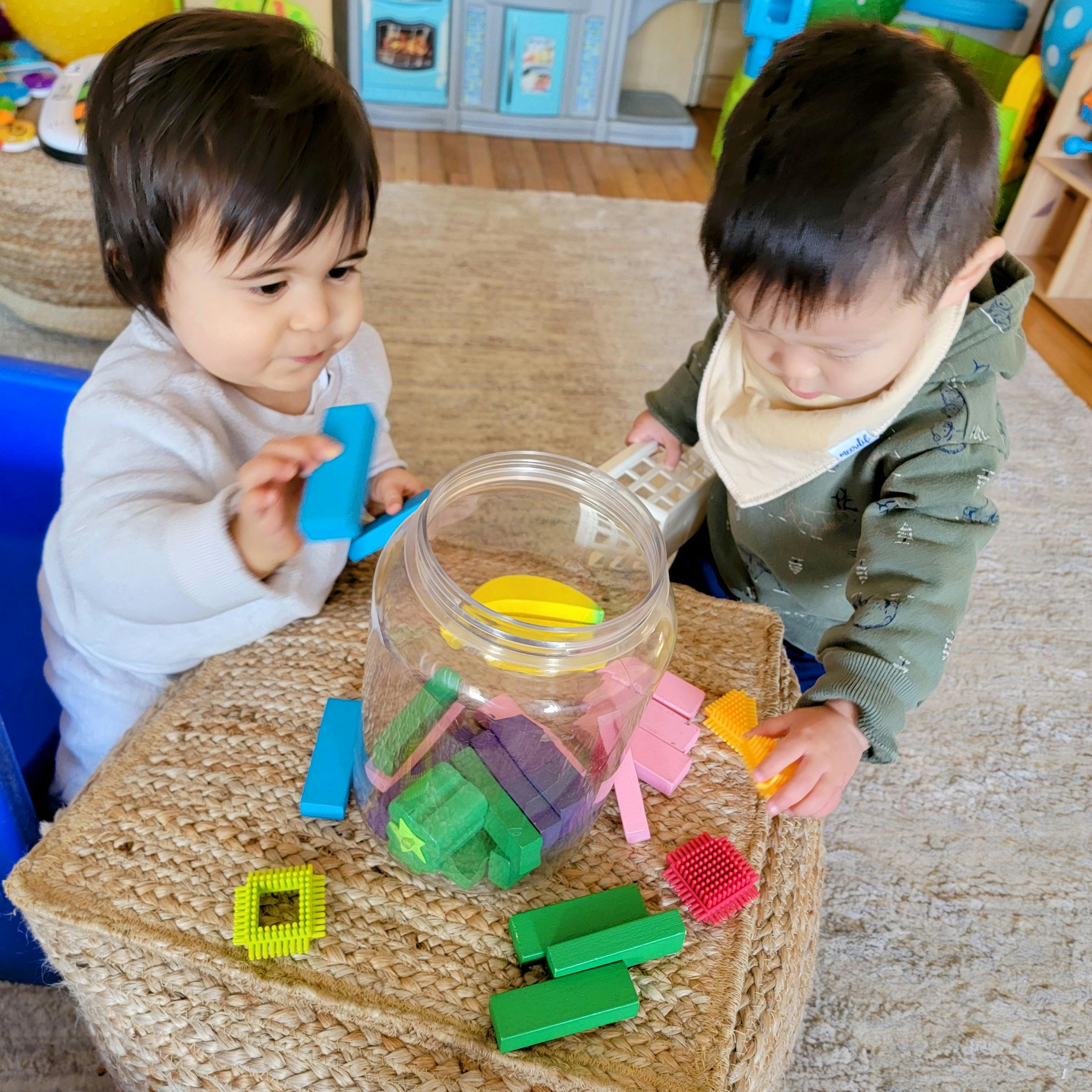 Two children playing with colorful blocks and a clear jar
