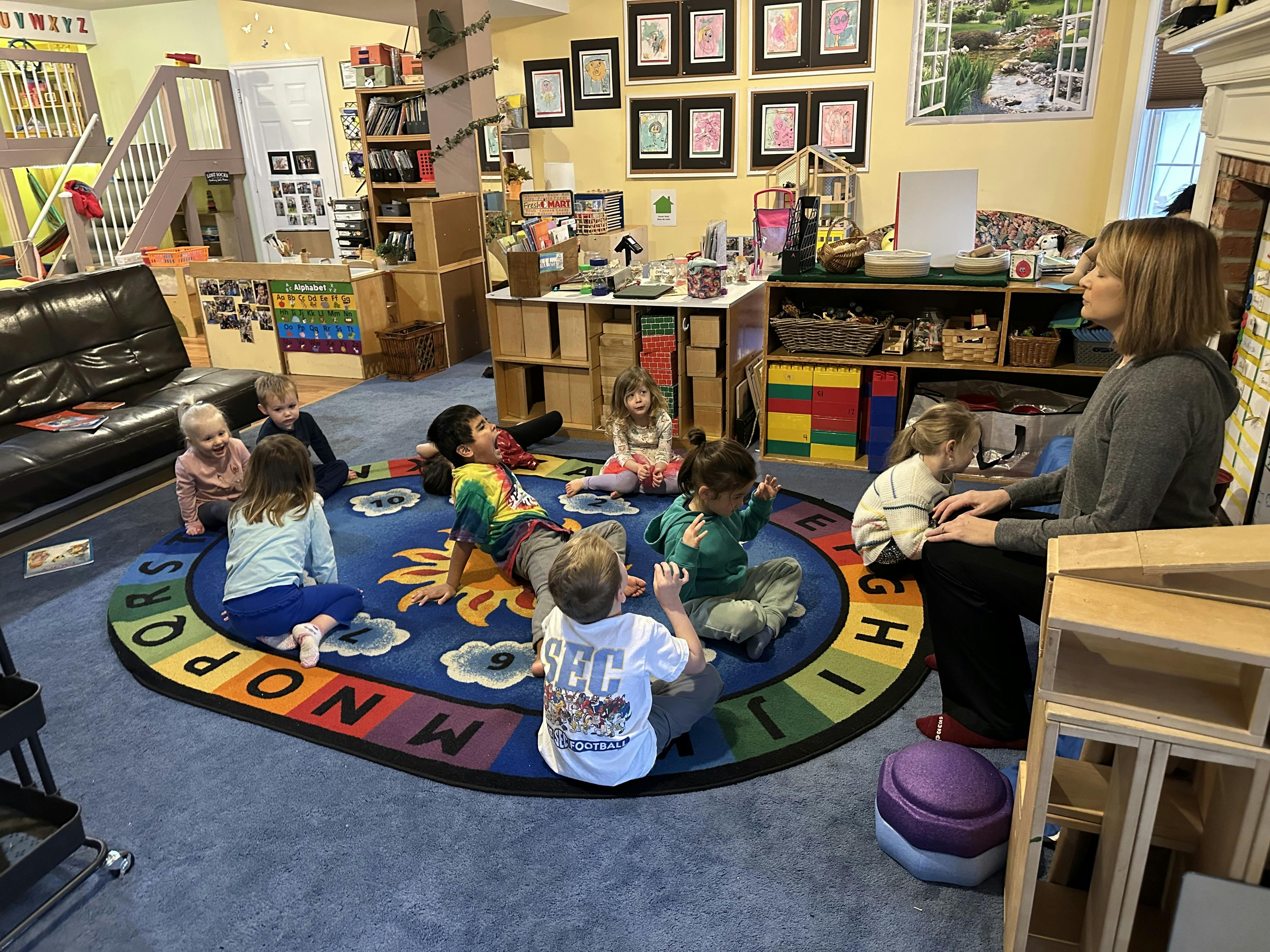 Teacher and children sitting on a colorful alphabet rug in a classroom