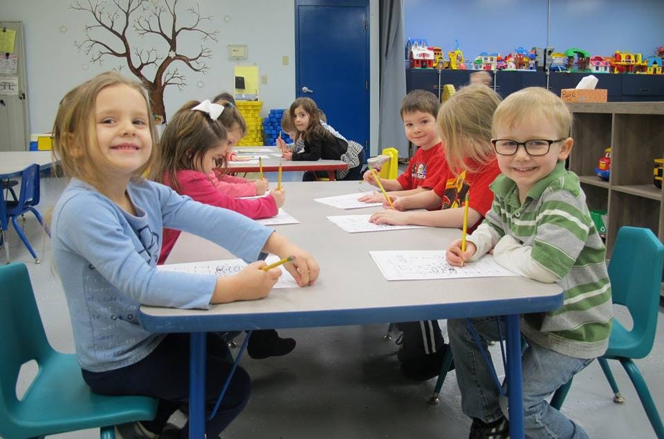 Children sitting at a table drawing with pencils