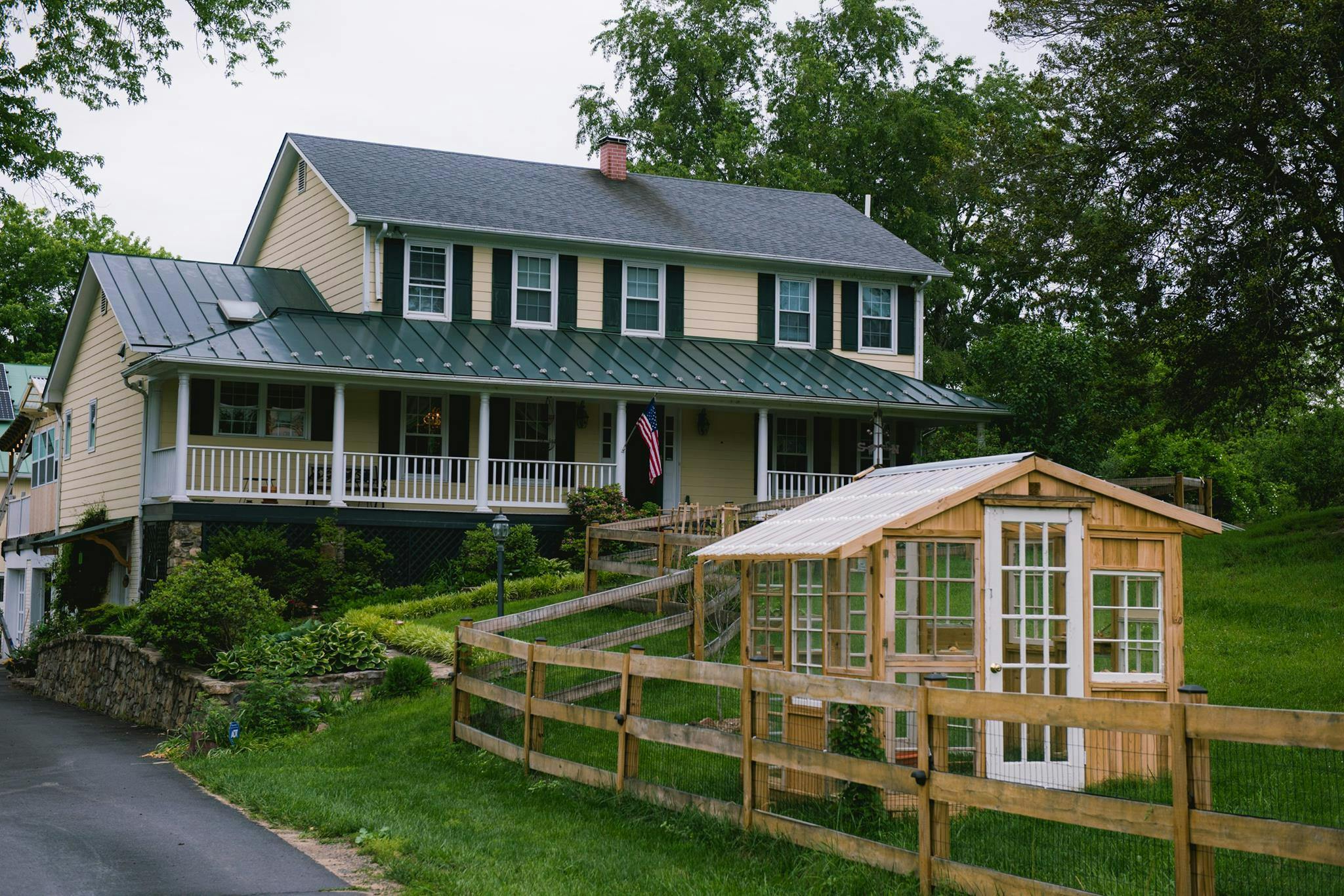 Two-story house with a porch and a small wooden structure with a fence