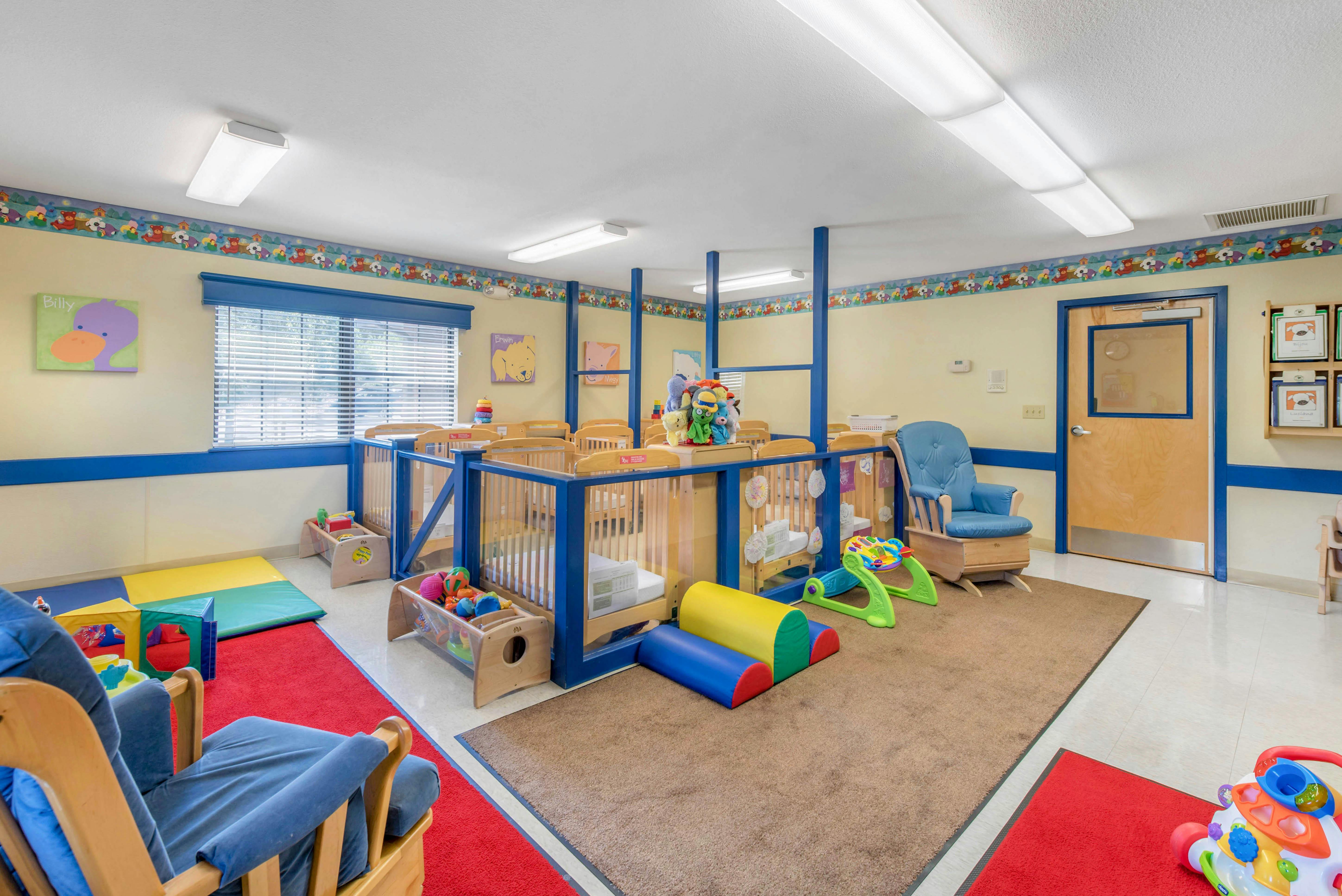 Baby room with multiple cribs, chairs, colorful rugs, and various toys