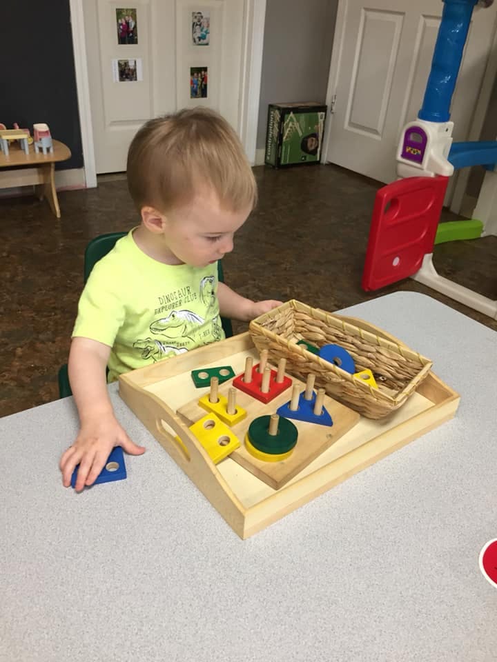 Child playing with a wooden shape sorting toy on a tray
