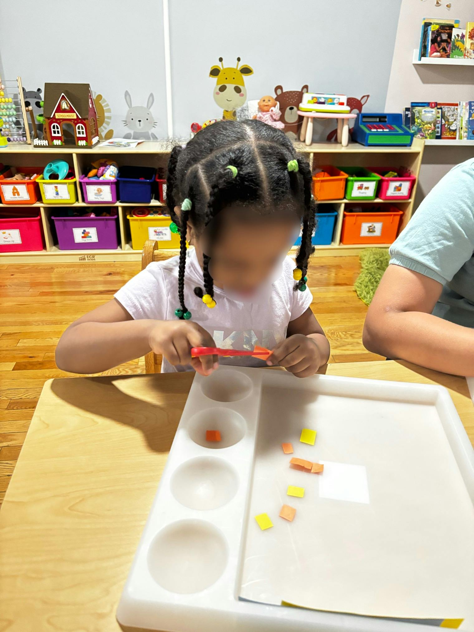 Child cutting small pieces of paper with scissors at a table in a classroom