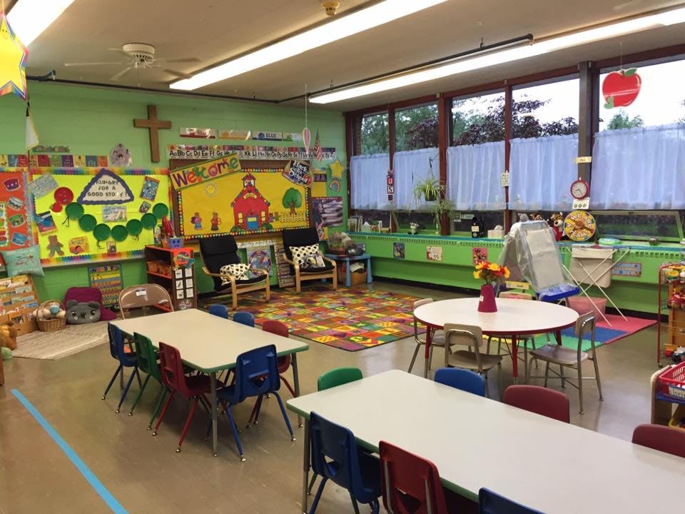 Classroom with small tables and chairs, colorful rug, and bulletin boards