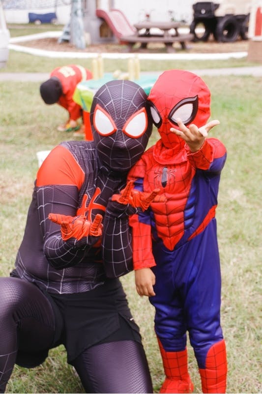 Person and child wearing spider hero costumes on a grassy field