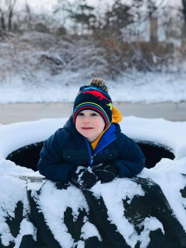 Child in a winter hat and coat sitting in a snow-covered tire