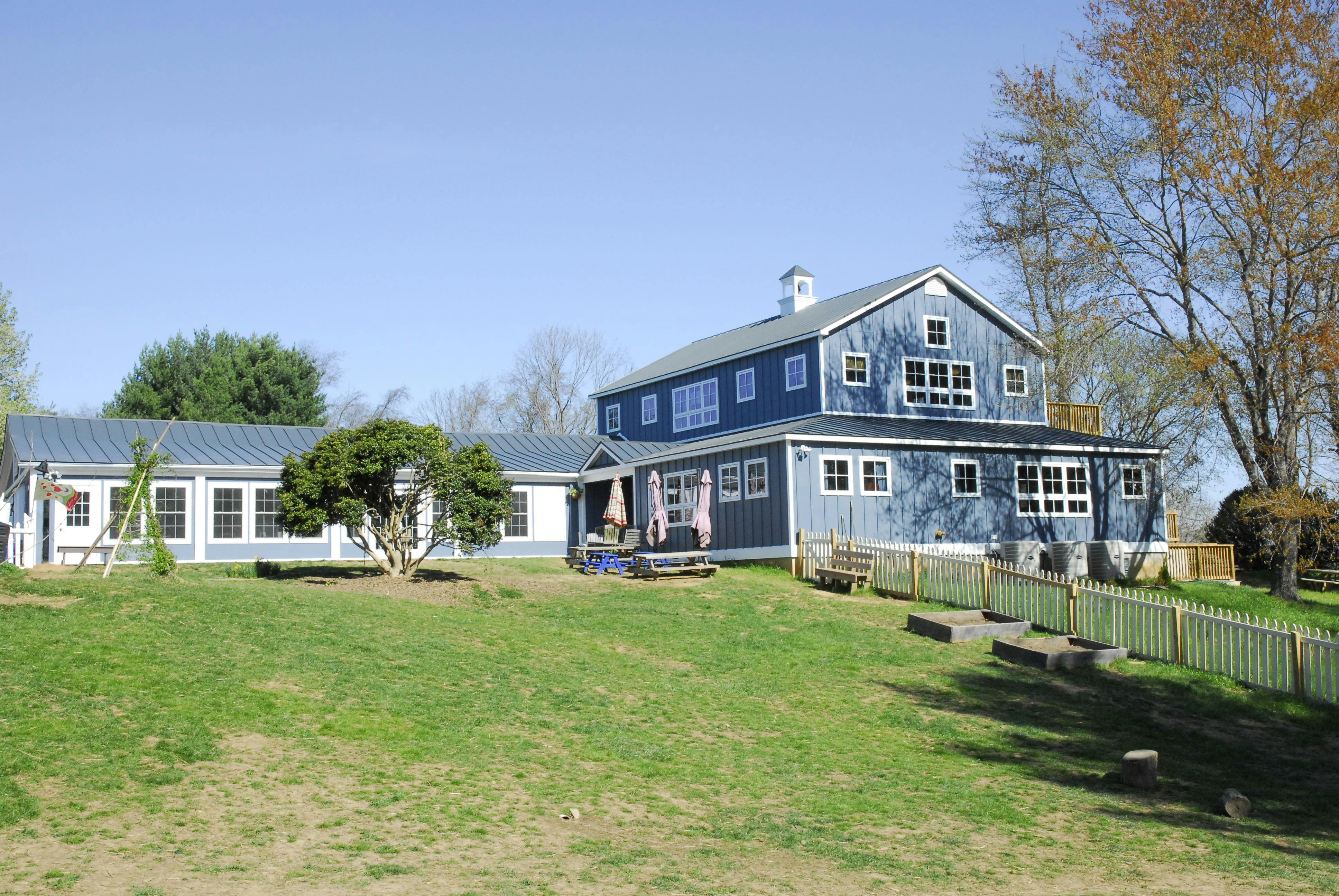 Blue barn-style building with white trim and a long white building next to it