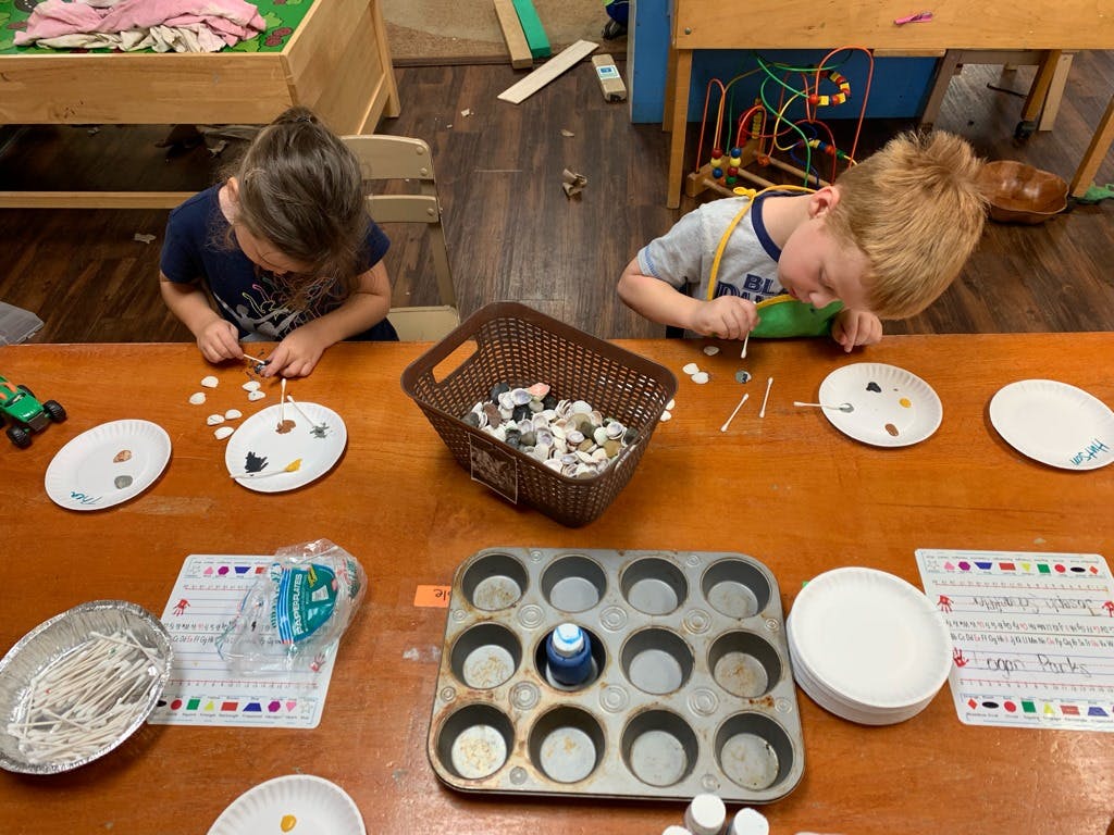 Two children at a table sorting small objects onto plates