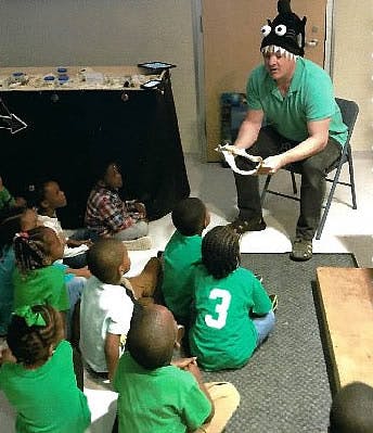 Person in a monster hat showing an object to children sitting on the floor