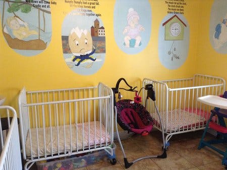 Two cribs and a baby swing in a room with cartoon wall decals