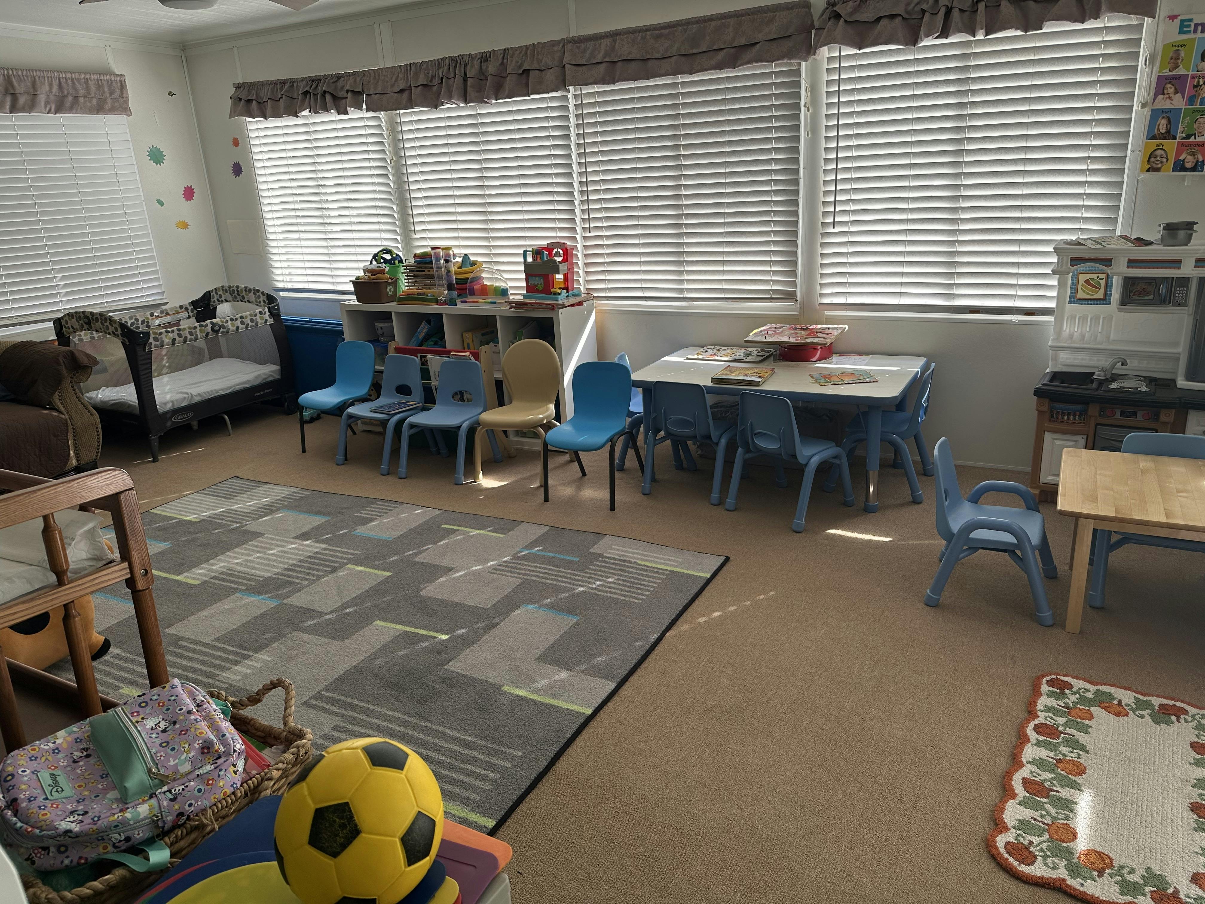 A playroom with small tables, chairs, a playpen, and shelves with toys