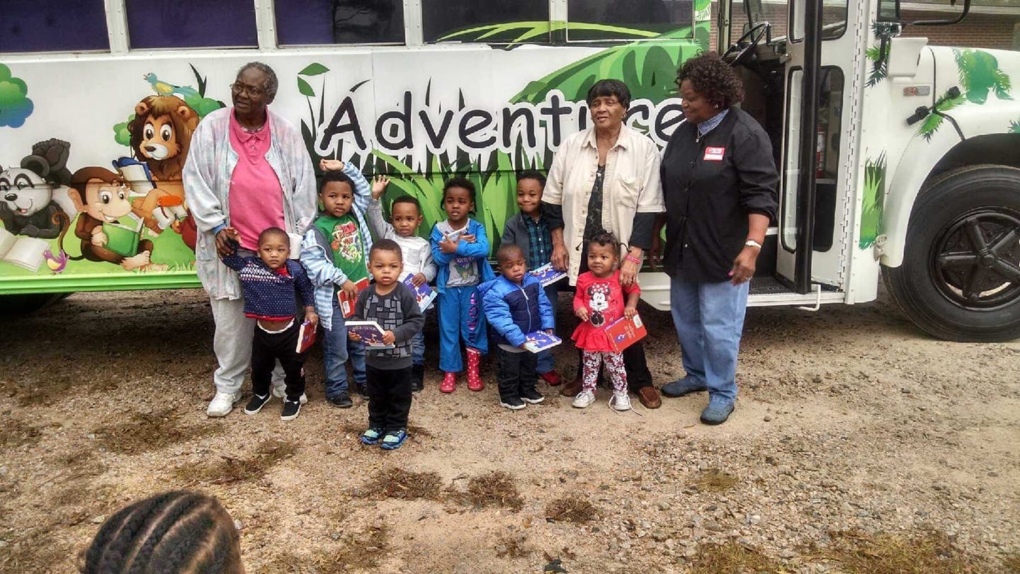 Adults and children standing in front of a bus with "Adventure" written on it