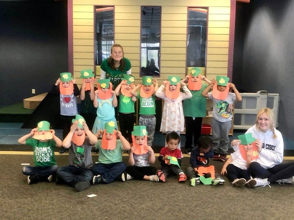 Group of children and adults holding up paper crafts to their faces