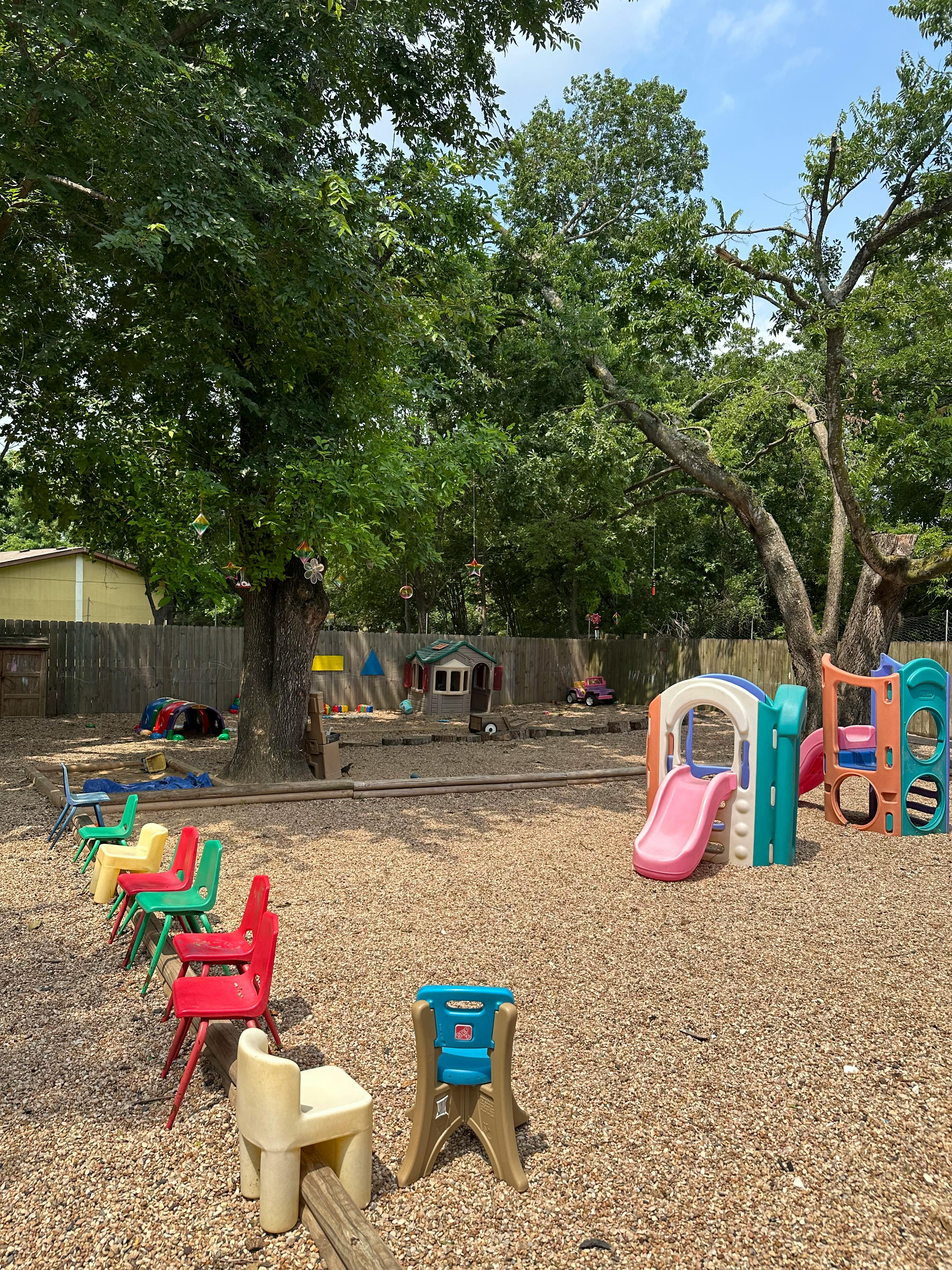 Outdoor playground with slides, play structures, and small chairs on wood chips