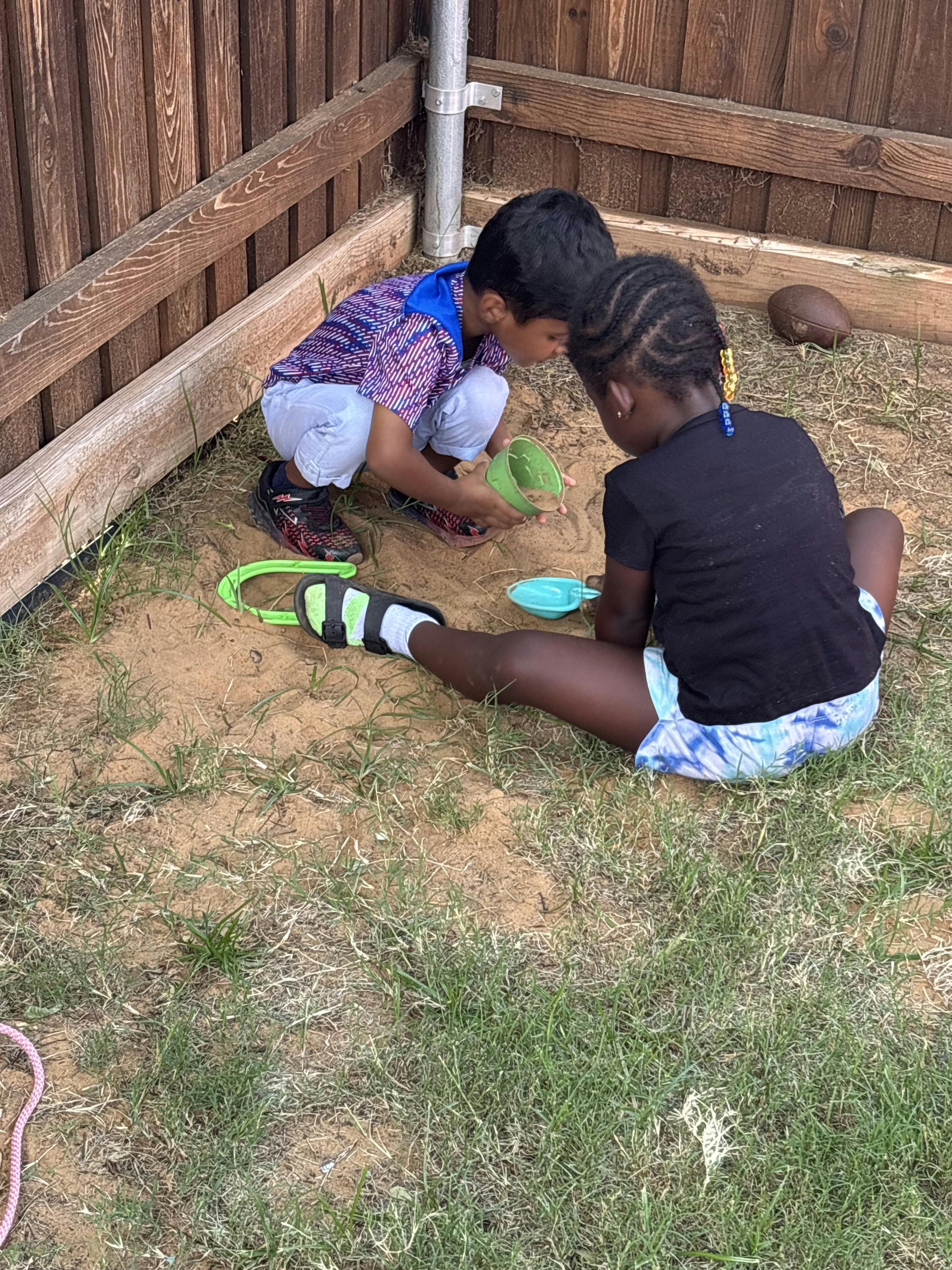 Two children playing in a sandbox with toys