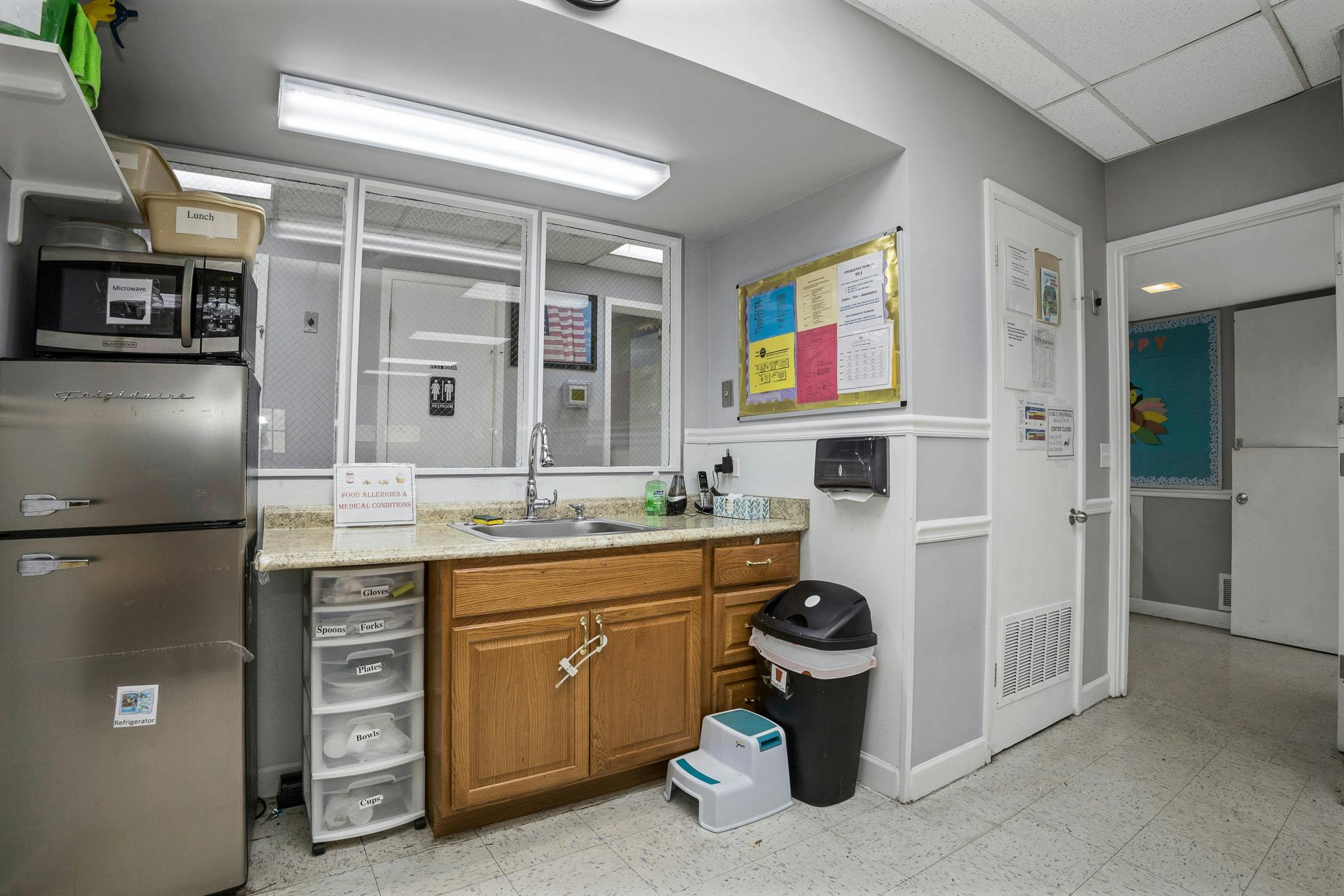 Kitchen area with a refrigerator, microwave, sink, cabinets, and step stool