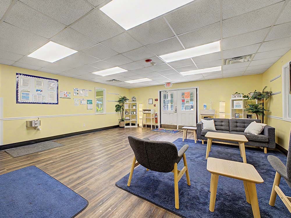 Lounge area in a school with blue rugs, chairs, sofa, and light wood tables