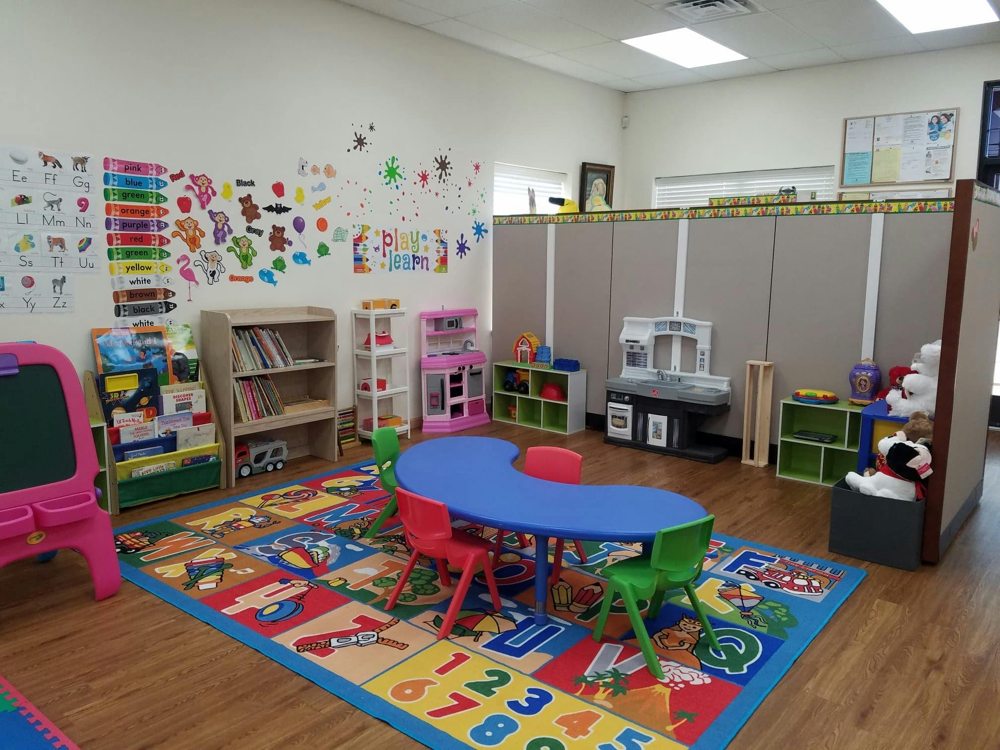 Children's classroom with a blue table, colorful rug, and drawings on the wall