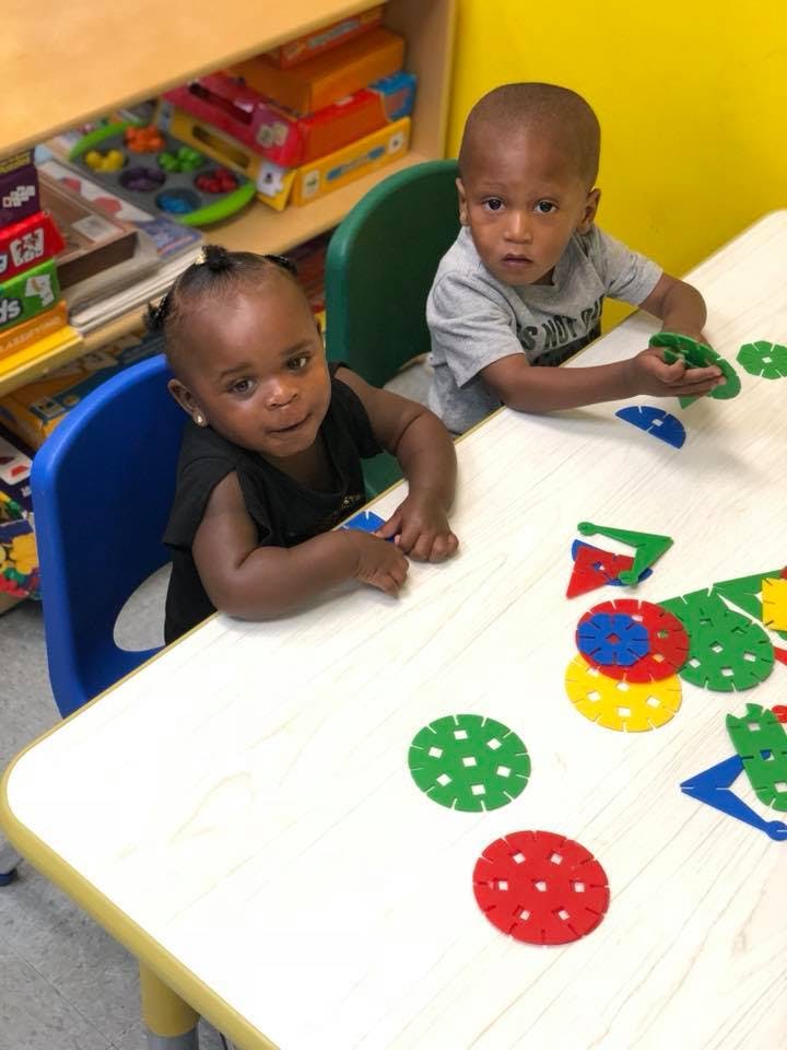 Two children playing with colorful interlocking plastic shapes at a table
