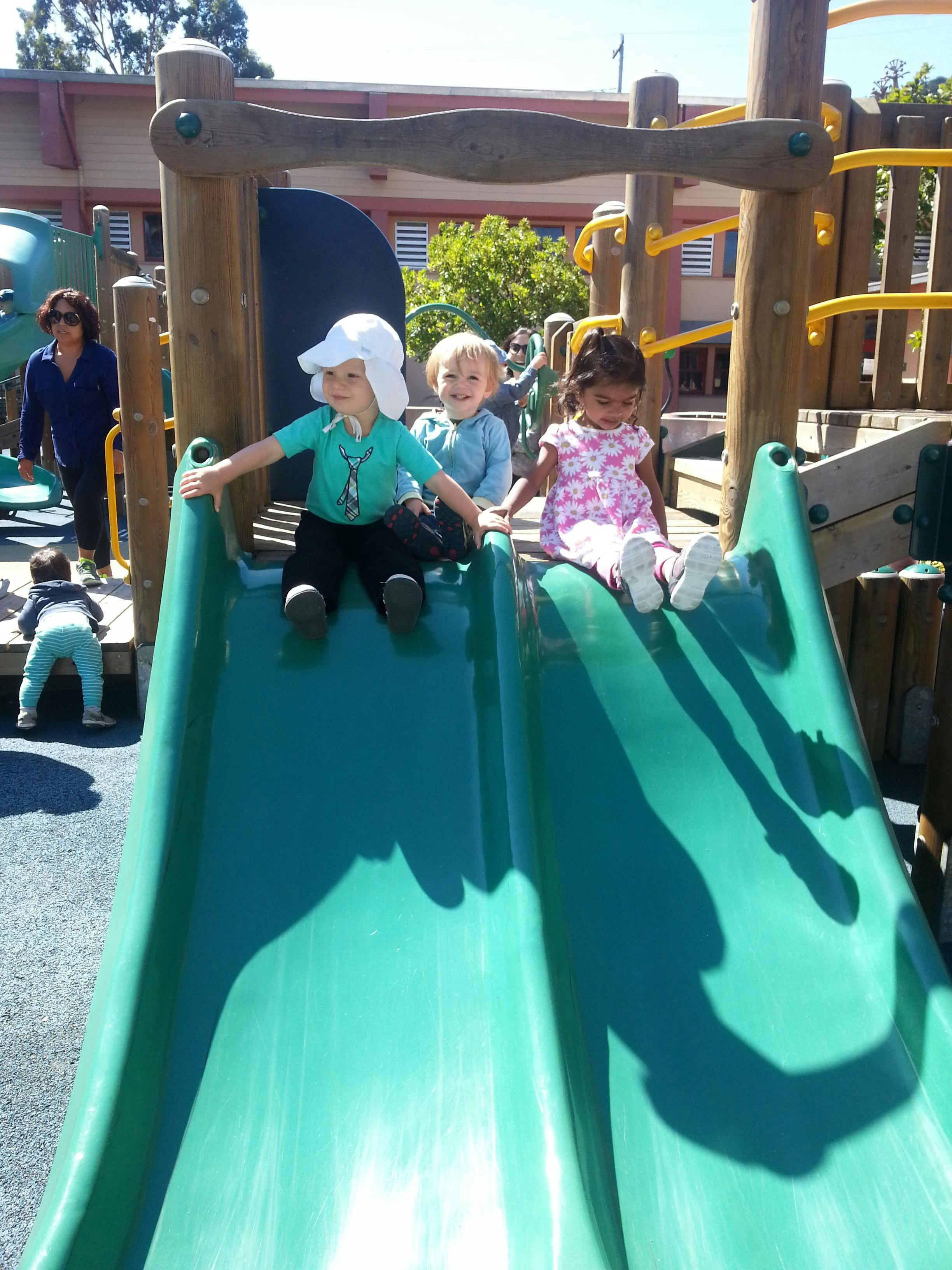 Three children sitting at the top of a playground slide