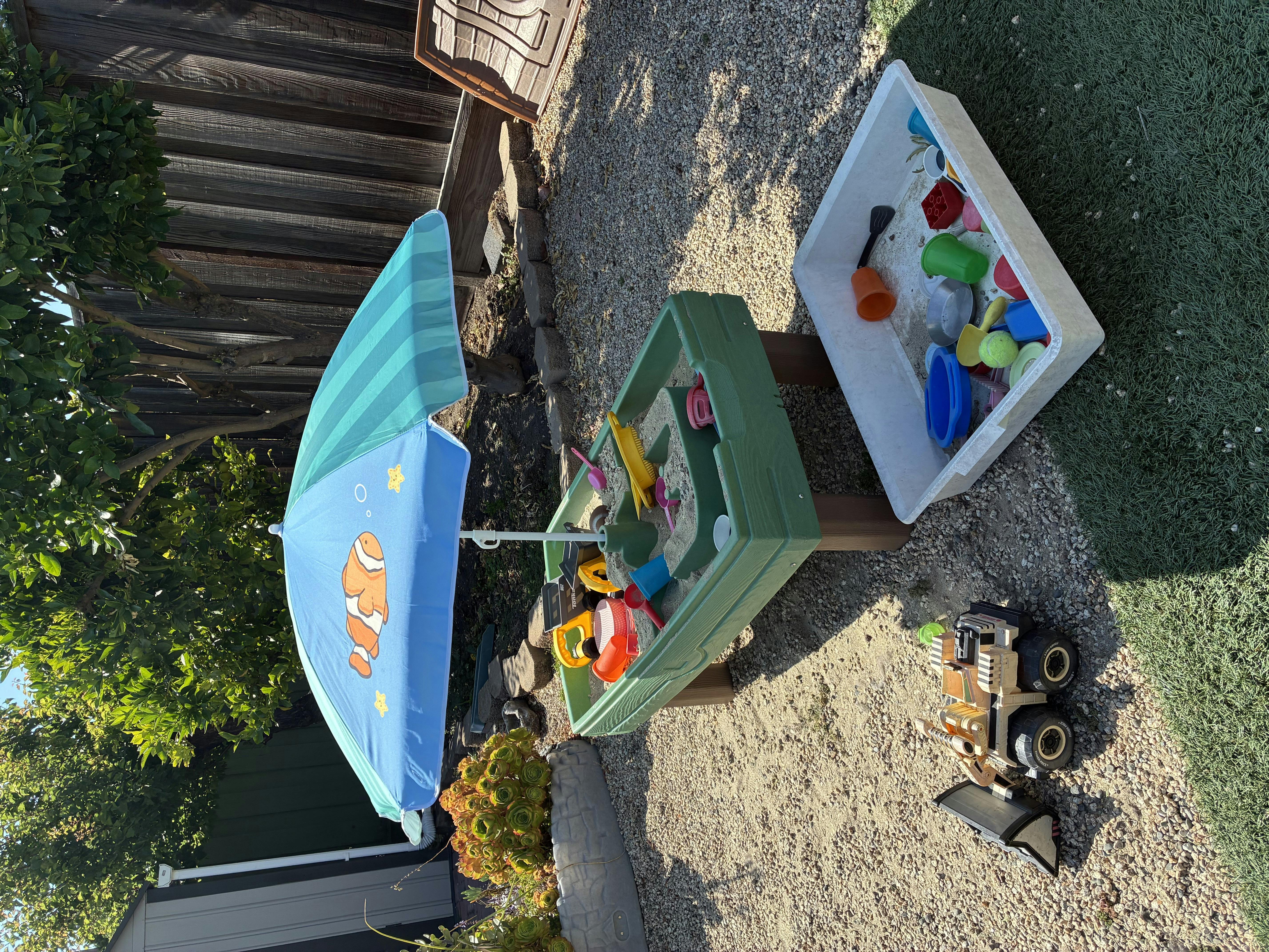 Sandbox and water table with toys and a blue umbrella