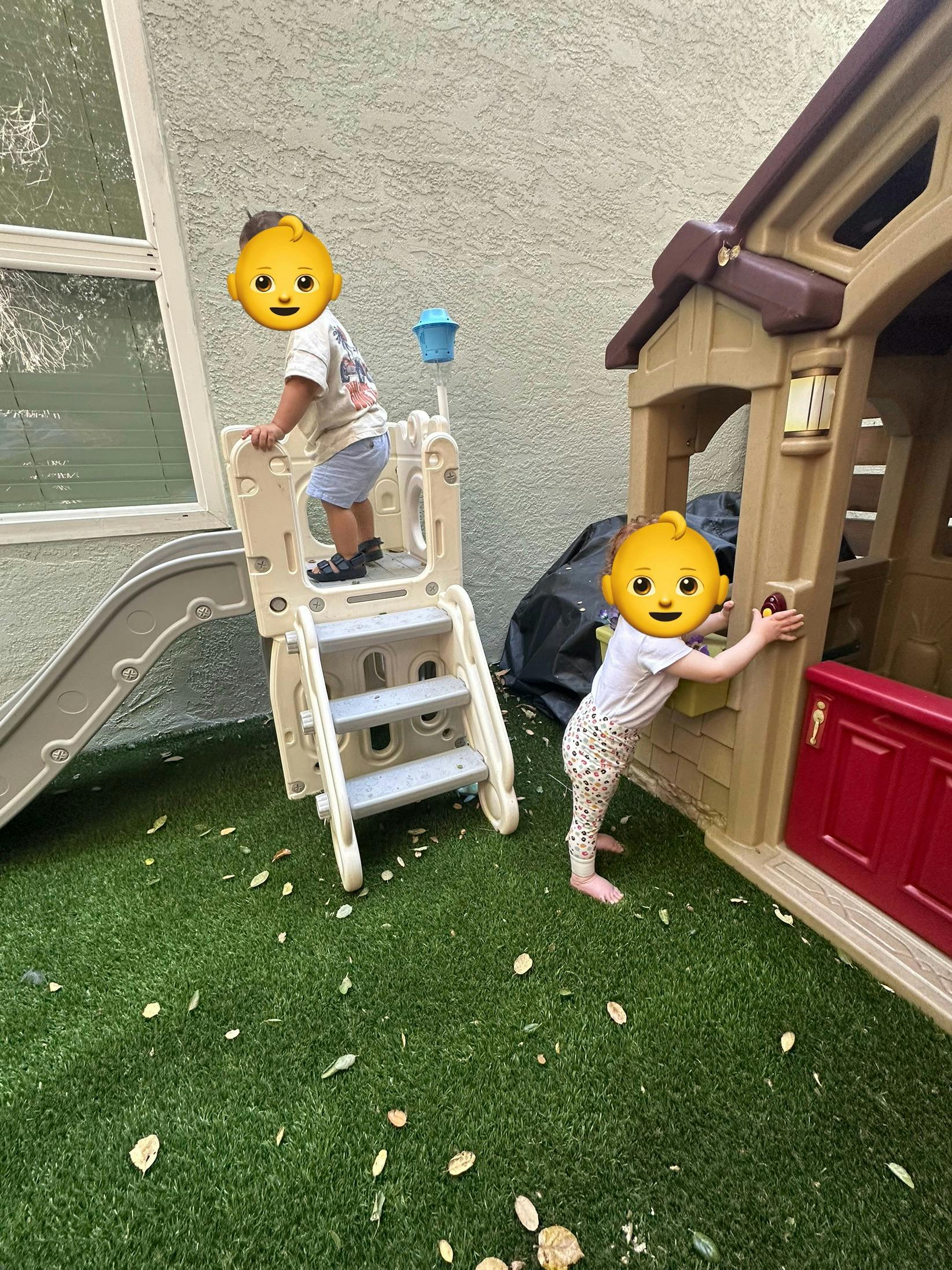 Two children playing on an outdoor slide and playhouse