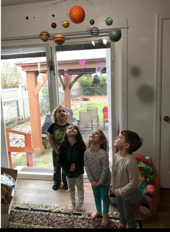 Four children looking up at a hanging solar system mobile